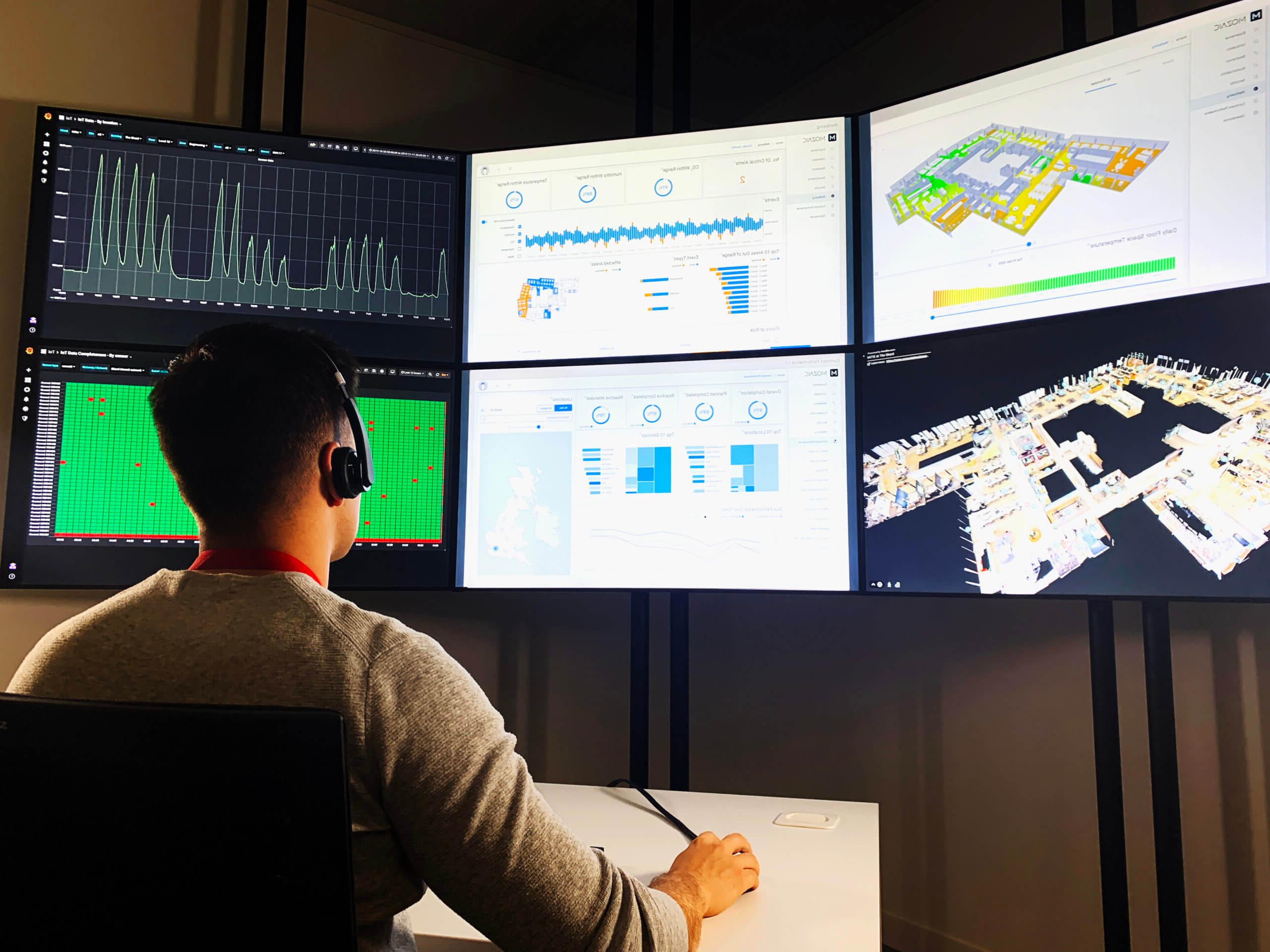 Man sitting in front of several laptop screens, showing various graphs and maps