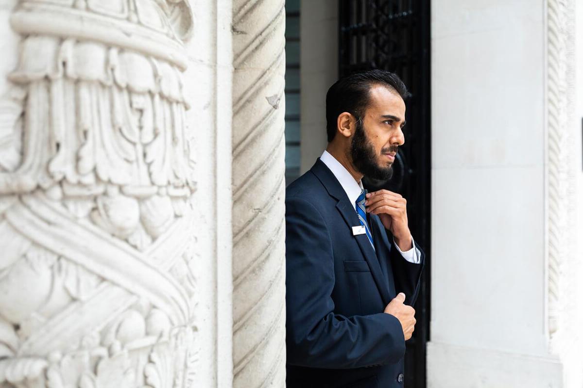 Security guard wearing a dark suit standing in a white marble doorway